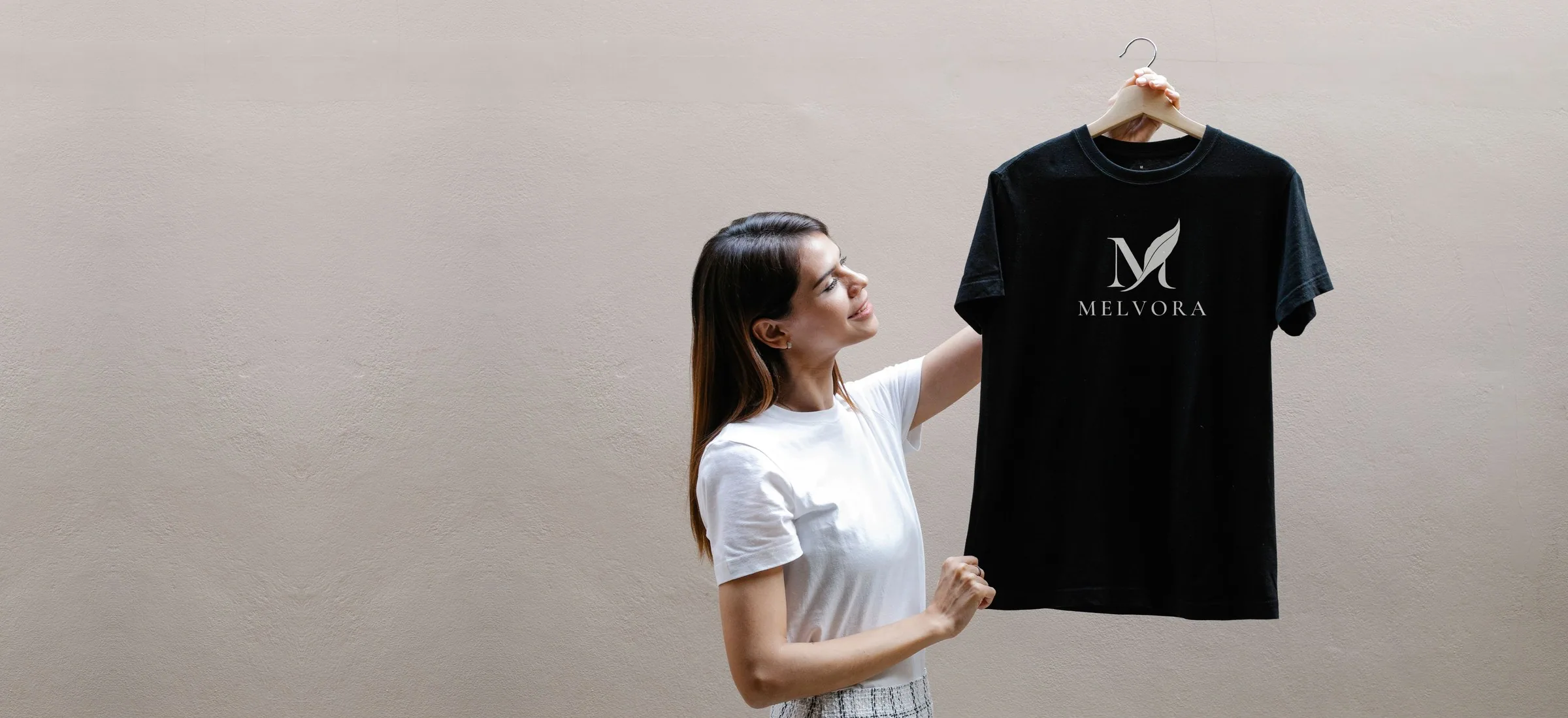 Woman holding up a black T-shirt printed with the MELVORA logo
