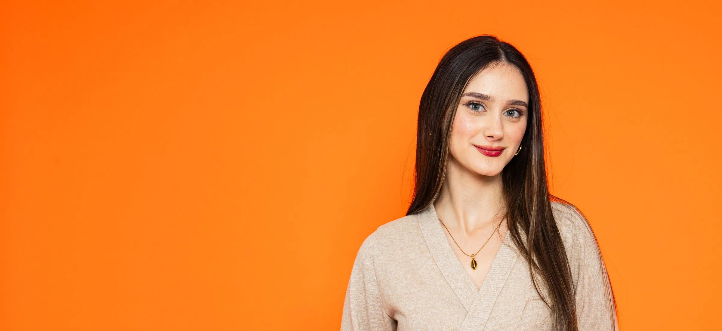 Smiling woman in a soft wrap top against a bright orange backdrop
